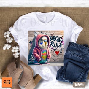 This isn't your average bird tee. Meet the boldest budgie on the block—rocking a pink hoodie and leaving her mark on the city walls with a freshly tagged “Budgies Rule” and a heart underneath. Perched confidently in front of her brick-wall masterpiece, this graffiti-loving parakeet is the perfect blend of cute, clever, and a little rebellious. Whether you're a bird mom, a graffiti fan, or just like your humor feathered and fierce, this tee brings the attitude—loud, proud, and a little punk rock.