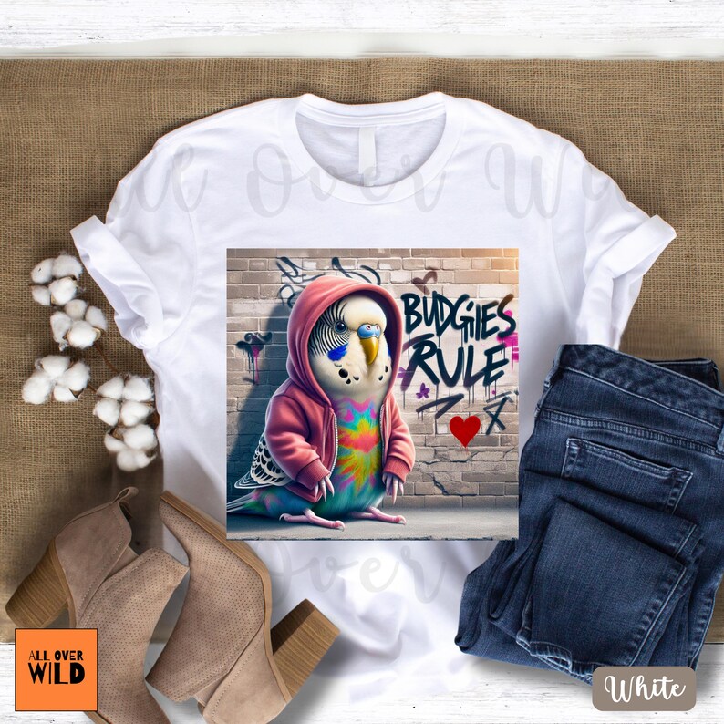 This isn't your average bird tee. Meet the boldest budgie on the block—rocking a pink hoodie and leaving her mark on the city walls with a freshly tagged “Budgies Rule” and a heart underneath. Perched confidently in front of her brick-wall masterpiece, this graffiti-loving parakeet is the perfect blend of cute, clever, and a little rebellious. Whether you're a bird mom, a graffiti fan, or just like your humor feathered and fierce, this tee brings the attitude—loud, proud, and a little punk rock.