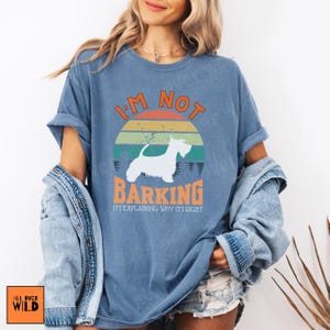 May include: A blue short-sleeve t-shirt featuring a graphic of a white dog silhouette against a retro-style sunset. The text reads I'M NOT BARKING I'M EXPLAINING WHY I'M RIGHT in orange and white lettering. The shirt has a crew neck and a relaxed fit.