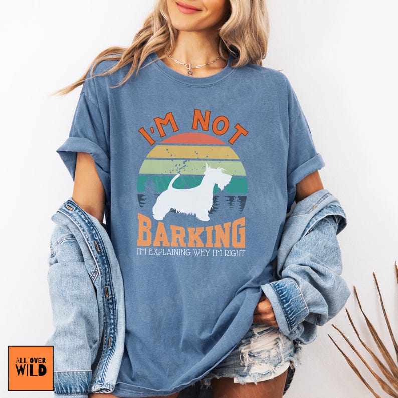 May include: A blue short-sleeve t-shirt featuring a graphic of a white dog silhouette against a retro-style sunset. The text reads I'M NOT BARKING I'M EXPLAINING WHY I'M RIGHT in orange and white lettering. The shirt has a crew neck and a relaxed fit.