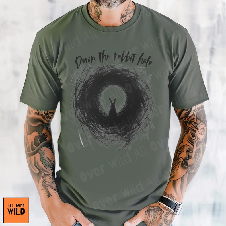May include: Olive green t-shirt with a black graphic of a rabbit silhouette in a swirling vortex, and the words "Down the rabbit hole". The shirt has short sleeves and a crew neck.