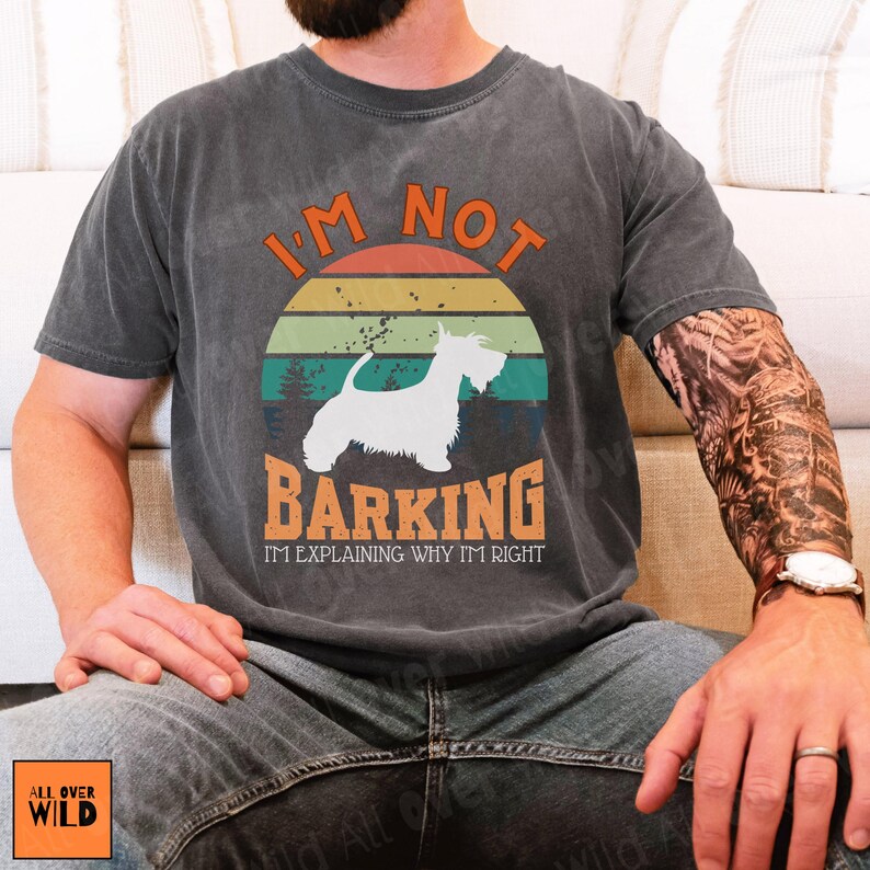 May include: A charcoal gray short-sleeve t-shirt featuring a graphic of a white dog silhouette centered within a vintage-style sunset circle. The text reads I'M NOT BARKING I'M EXPLAINING WHY I'M RIGHT in orange and white lettering.