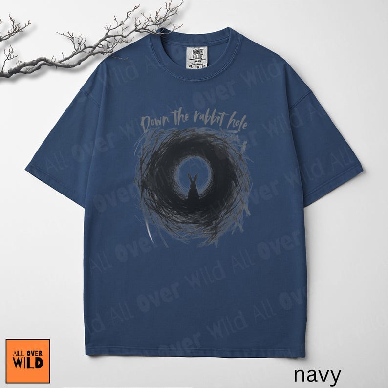 May include: Navy blue t-shirt featuring a rabbit silhouette in a dark hole, with the text "Down the rabbit hole". The shirt has a crew neck and short sleeves. The brand logo "All Over Wild" is in the bottom left corner.