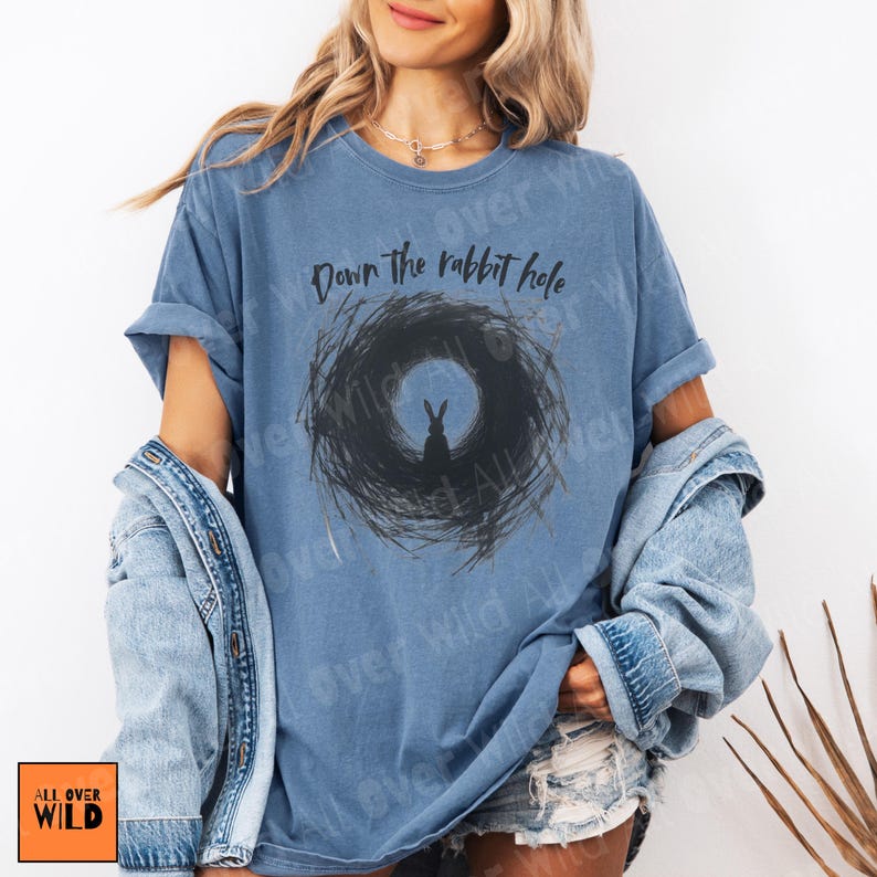 May include: A blue t-shirt featuring the phrase "Down the rabbit hole" above a black rabbit graphic within a circular design. The shirt is from the "All Over Wild" collection.