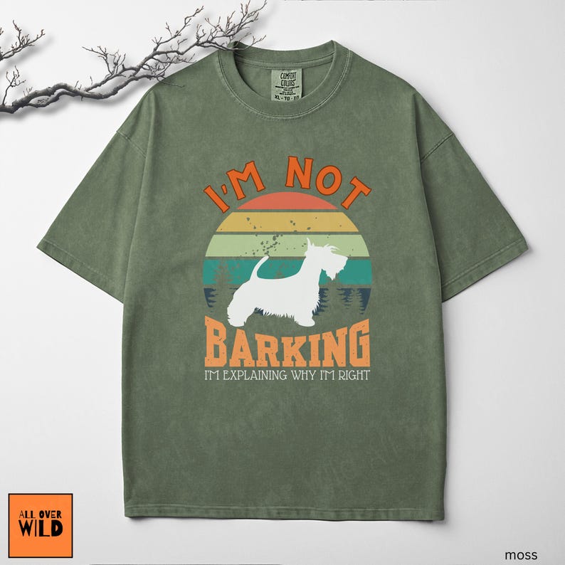 May include: A moss green t-shirt featuring a graphic of a white dog silhouette centered over a retro-style sunset circle. The text reads I'M NOT BARKING I'M EXPLAINING WHY I'M RIGHT in orange and white lettering. The shirt has a crew neck design.