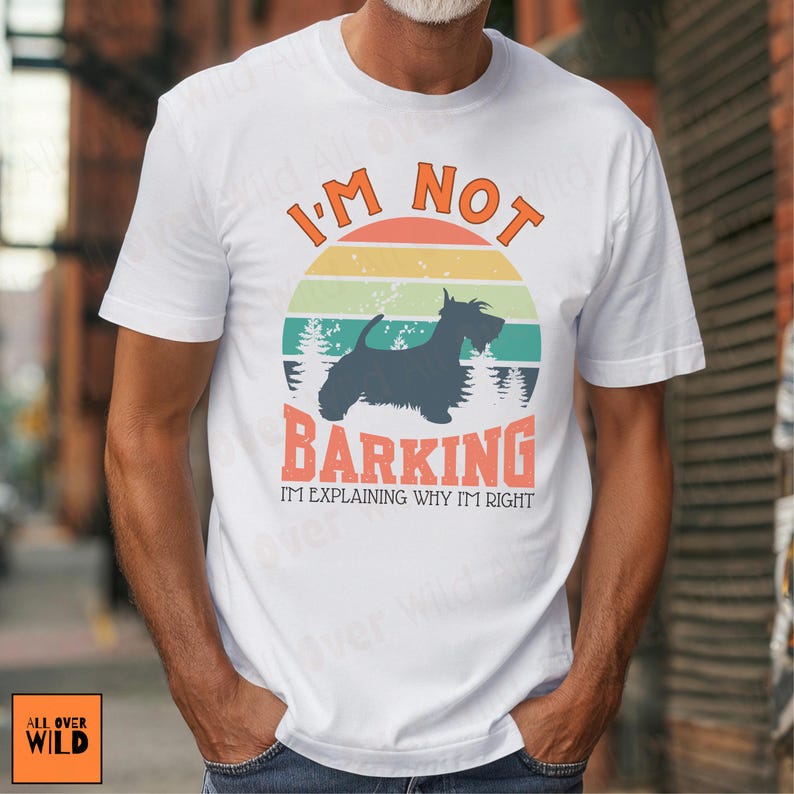 May include: A white short-sleeved t-shirt featuring a graphic of a black Scottish Terrier silhouette against a retro-style sunset circle. The text reads I'M NOT BARKING I'M EXPLAINING WHY I'M RIGHT in orange and black block lettering.