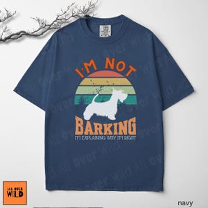 May include: A navy blue short-sleeve t-shirt featuring a graphic of a white dog silhouette against a sunset background. The text reads I'M NOT BARKING I'M EXPLAINING WHY I'M RIGHT in orange and white lettering. The shirt has a crew neckline.