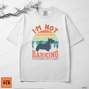 May include: A white short-sleeve t-shirt featuring a graphic of a black Scottish Terrier silhouette against a retro sunset circle. The text reads I'M NOT BARKING I'M EXPLAINING WHY I'M RIGHT in orange and black lettering with a forest background.