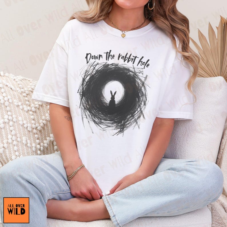 May include: White t-shirt with a black and white illustration of a rabbit in a tunnel, and the words "Down the rabbit hole". The tee has a round neck and short sleeves.