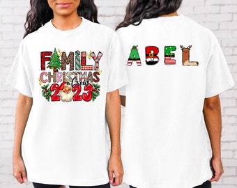 May include: White t-shirt with a festive Christmas design on the front that says "Family Christmas Crew 2023". The back of the shirt has the name "ABEL" spelled out in colourful letters with Christmas-themed embellishments.