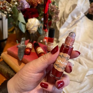 May include: A red glass bottle with a rollerball applicator and a gold label that says "Astarian". The bottle is filled with a red liquid and has glitter inside.