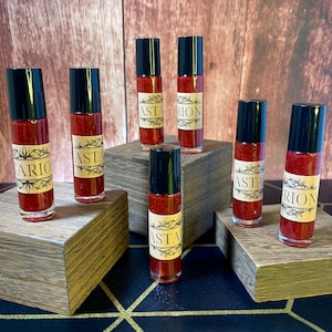 May include: Seven small glass bottles with black caps and red liquid inside. The bottles are arranged in a staggered pattern on wooden blocks. The labels on the bottles read "Astarion" and "Asta".