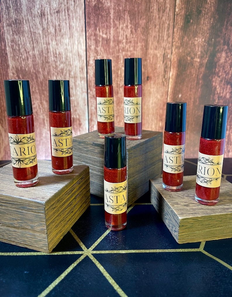 May include: Seven small glass bottles with black caps and red liquid inside. The bottles are arranged in a staggered pattern on wooden blocks. The labels on the bottles read "Astarion" and "Asta".