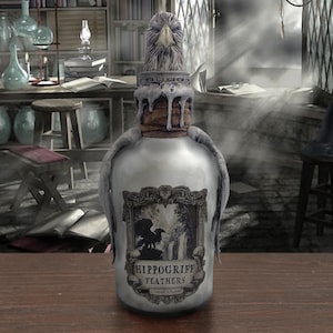 Puede incluir: Una botella plateada con un tapón esculpido en forma de cabeza de hipogrifo. La botella tiene una etiqueta que dice "Hippogriff Feathers".