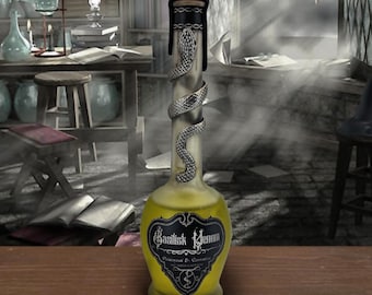 Peut inclure: Une bouteille décorative en verre contenant un liquide jaune, étiquetée "Venin de Basilic". Un serpent argenté est enroulé autour du col de la bouteille, qui est scellée avec un bouchon noir. La bouteille est posée sur une surface en bois.