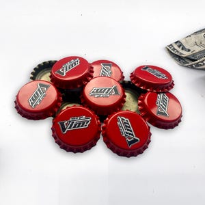 以下が含まれることがあります： 「Vim!」と書いてある黒と白のロゴがついた赤いボトルキャップが10個あります。