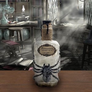 Puede incluir: Una botella de vidrio decorativa con la inscripción "Acrormantula Spider Silk". La botella presenta un diseño de araña negra y está envuelta con cuerda. El tapón es oscuro y la botella está sobre una superficie de madera.