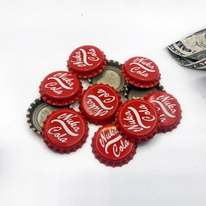 May include: A pile of red bottle tops with white lettering that reads "Nuka Cola".