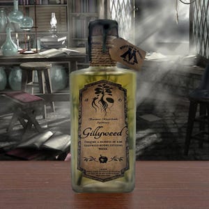 Puede incluir: Una botella de vidrio transparente llena de un líquido verde claro, con una etiqueta de estilo vintage que dice Gillyweed, Beaumont Marjoribanks Apothecary y Ministry of Magic Approved. El tapón de corcho está sellado con cera negra y envuelto en cuerda.