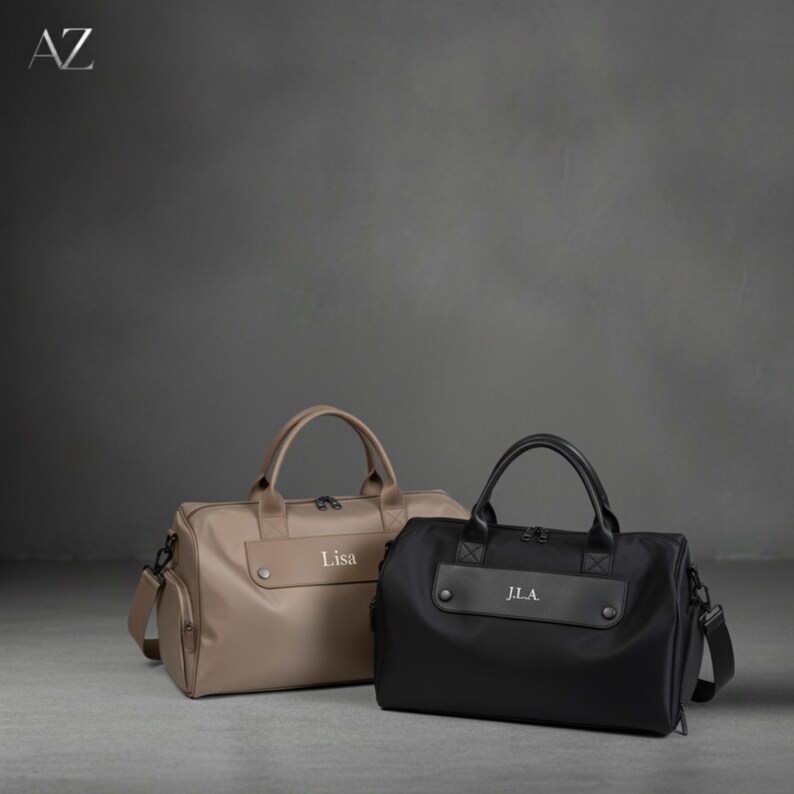 May include: Two personalized duffel bags. One is tan with the name "Lisa" and the other is black with "J.L.A." Both have top handles, side pockets, and shoulder straps. The bags are on a gray surface with a dark gray background.