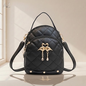 Puede incluir: Mochila acolchada negra con detalles dorados. Cuenta con un asa superior, correas ajustables para los hombros y una solapa frontal con un diseño de flamenco dorado. La bolsa tiene un patrón de diamantes y un pequeño bolsillo con cremallera.