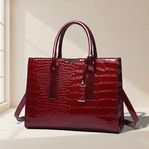 May include: A glossy, burgundy-colored handbag with a crocodile-skin texture. The bag features two top handles and a detachable shoulder strap. The hardware is silver-toned, and the bag has a rectangular shape.