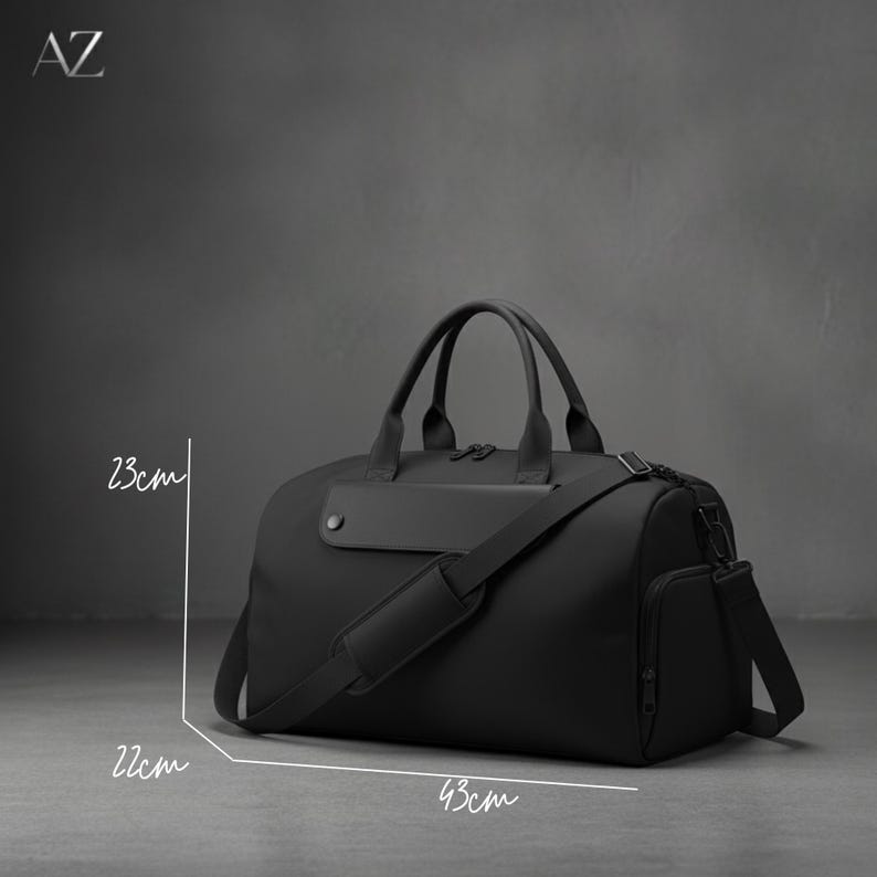 May include: A black duffel bag with a shoulder strap and handles. The bag is 43 cm long, 22 cm high, and 23 cm wide. It has a side pocket and a flap with a button. The letters "AZ" are in the top left corner.