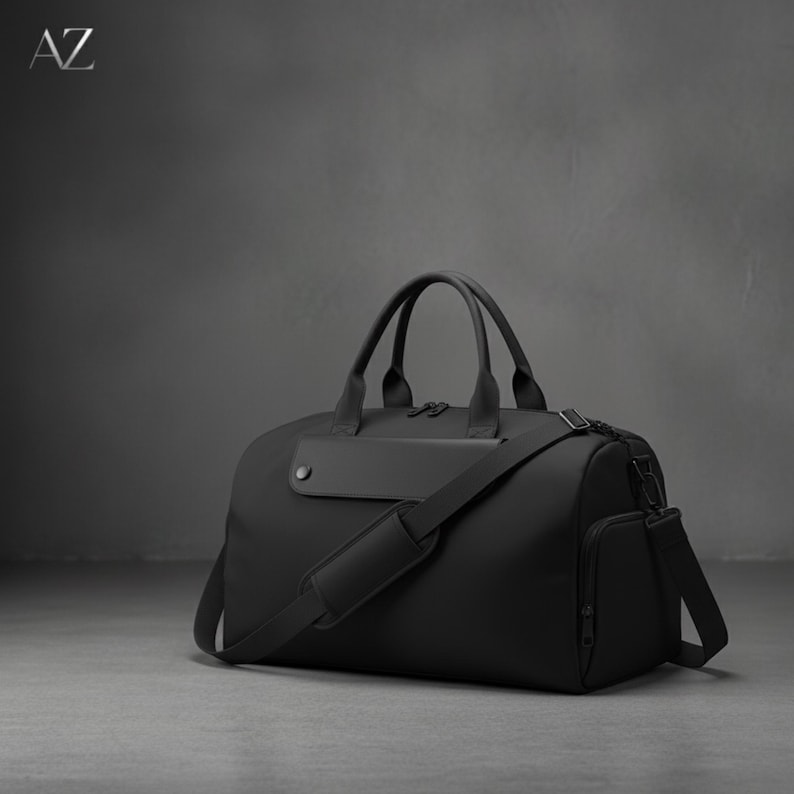May include: A black duffel bag with a shoulder strap and top handles. The bag has a rectangular shape with a side pocket and a small, rectangular patch on the front. The letters "AZ" are in the upper left corner.