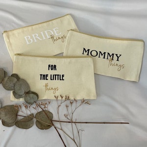 Könnte beinhalten: Drei beigefarbene Canvas-Reißverschlusstaschen mit schwarzem Text. Die Taschen tragen die Aufschrift "Bride things", "Mommy things" und "For the little things".