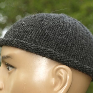 Op de afbeelding: Een donkergrijze gebreide beanie met een omgeslagen rand. De beanie is gemaakt van zacht, getextureerd garen.