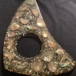 May include: A triangular-shaped decorative object made of resin with a circular opening in the center. The resin is embedded with iridescent, pearlescent, and gold-colored flakes and pieces.