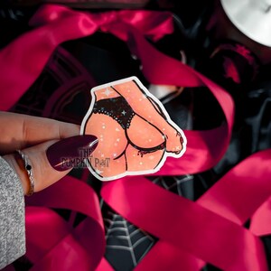 May include: A sticker featuring a stylized illustration of a person's lower body in black underwear with star accents. The sticker has a peach-colored skin tone and is surrounded by pink ribbons and a black background. The text "THE PUMPKIN POT" is visible.