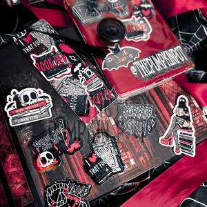 Op de afbeelding: Een verzameling stickers en een telefoonhoesje met een rode glitterachtergrond. De stickers tonen gotische en horrorthema's, waaronder schedels, boeken en de tekst "BOOKS THAT FUCK ME UP". Een zwarte kwast en rood lint zijn ook zichtbaar.
