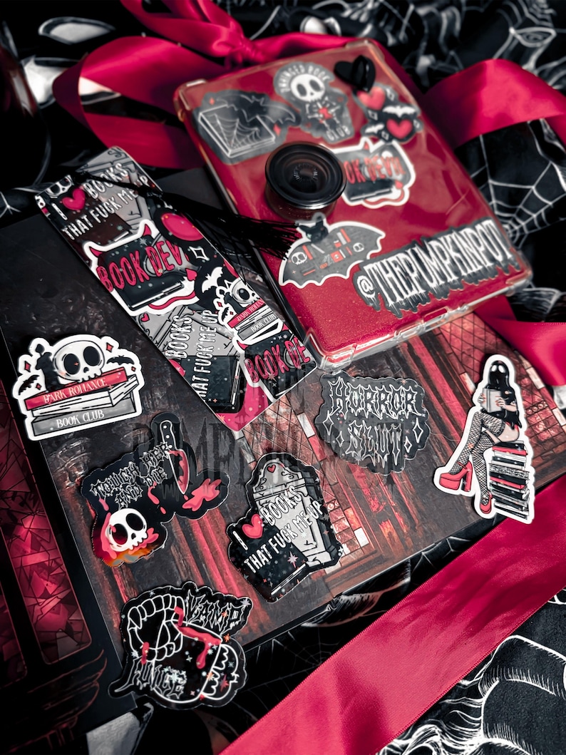 Op de afbeelding: Een verzameling stickers en een telefoonhoesje met een rode glitterachtergrond. De stickers tonen gotische en horrorthema's, waaronder schedels, boeken en de tekst "BOOKS THAT FUCK ME UP". Een zwarte kwast en rood lint zijn ook zichtbaar.