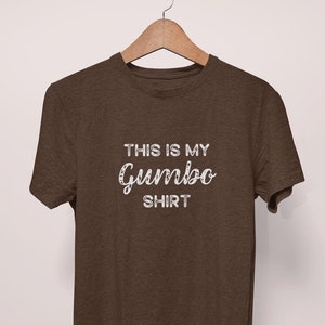 May include: A brown t-shirt with the text "This is my Gumbo Shirt" printed in white on the front.