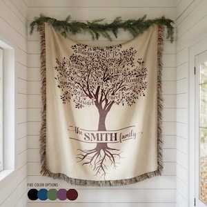 May include: A cream-colored woven throw blanket featuring a dark brown printed family tree design with names including Harper, BJ, Yvonne, Mike, Sammy, Becky, Renee, Stewart, and Carol. The text reads the SMITH family. It has fringed edges.
