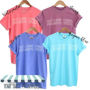 May include: Four t-shirts with the text "Beach Bum" in white on a variety of coloured backgrounds. The colours are watermelon, berry, lagoon blue, and flo blue.