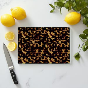 May include: A brown and black tortoiseshell patterned cutting board with a white border. The board is on a white marble surface with lemons and a knife.