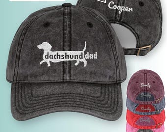 Puede incluir: Gorra de béisbol negra desgastada con las palabras "dachshund dad" y una silueta de perro salchicha bordada en blanco. La parte trasera de la gorra está personalizada con el nombre "Cooper". Se muestran opciones de color adicionales.