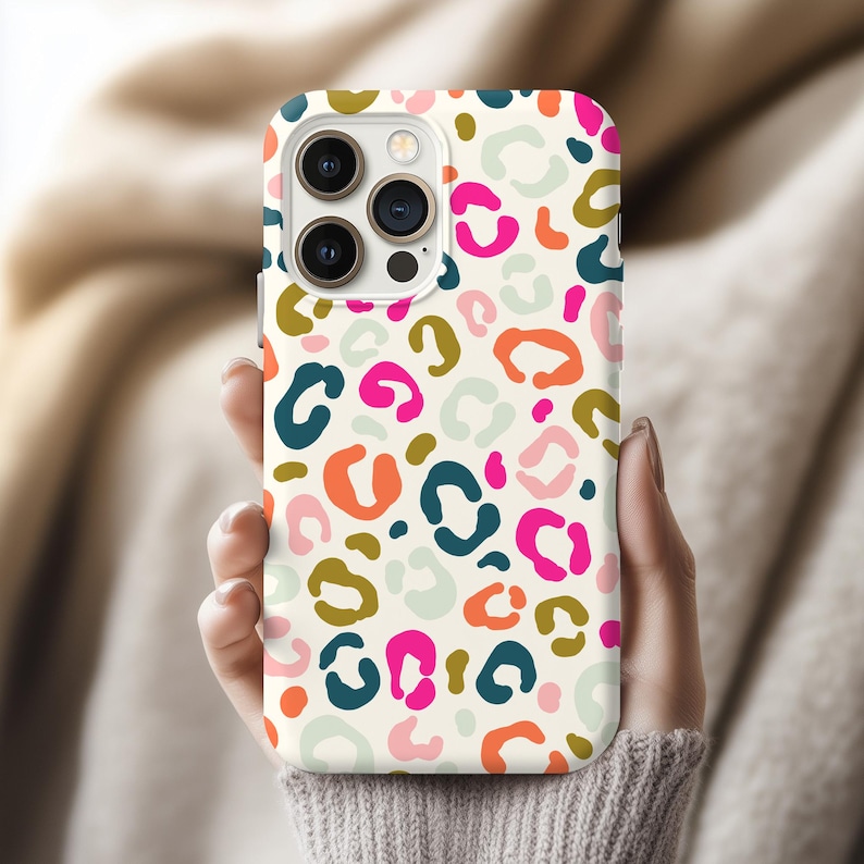 Puede incluir: Una funda para smartphone con un estampado de leopardo multicolor sobre un fondo crema. El dise&ntilde;o incluye manchas irregulares en tonos rosa intenso, verde azulado oscuro, verde oliva, naranja y verde menta p&aacute;lido, con un recorte para triple c&aacute;mara.