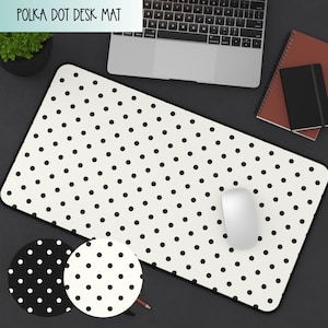 Pode incluir: Tapete de mesa retangular com fundo creme e bolinhas pretas. O tapete tem uma borda preta e o texto "POLKA DOT DESK MAT" na parte superior. Um mouse de computador branco está no tapete. Uma pequena imagem circular mostra o padrão de bolinhas.