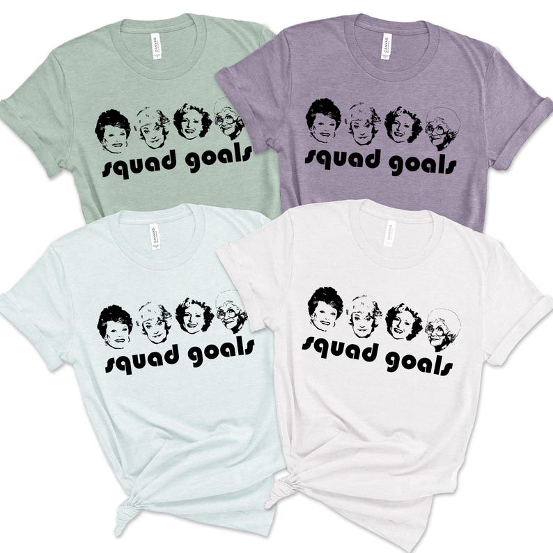 May include: Four t-shirts in shades of green, lilac, and white. Each shirt features a black graphic of five women's faces and the words "squad goals" in a black, bold font. The shirts are casual and have short sleeves.