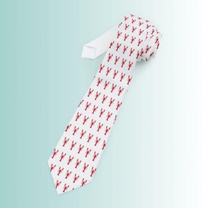 Op de afbeelding: Een witte stropdas met een herhaald patroon van rode kreeften. De stropdas staat schuin, waardoor het kreeftenontwerp over de hele lengte te zien is. De achtergrond is een verloop van lichtblauw en wit.