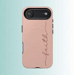 Pu&ograve; includere: Una custodia per telefono rosa antico con un alloggiamento per fotocamera nero. La parola "faith" &egrave; scritta in corsivo sulla custodia. La custodia ha una finitura liscia e un design protettivo.