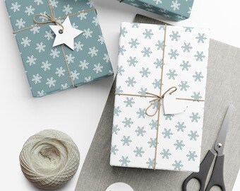 May include: Gift boxes wrapped in snowflake patterned paper, tied with twine and adorned with star-shaped tags. One box is teal with white snowflakes, another is white with teal snowflakes. The image includes a ball of twine and scissors.