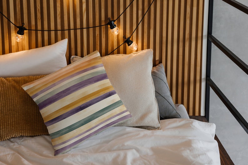 May include: A white bed with a striped pillow, a beige pillow, a brown corduroy pillow, and a white pillow. The bed is against a wood wall with string lights.