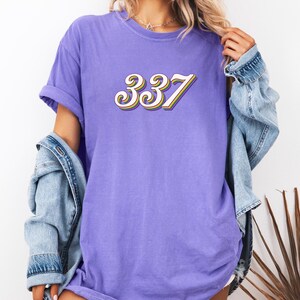 May include: A purple t-shirt with the number 337 in a retro, white, yellow, and orange font.