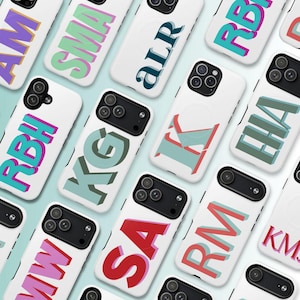 Puede incluir: Una colección de fundas blancas para smartphone con varios monogramas de letras en bloque tridimensionales en diversas combinaciones de colores como rosa, turquesa, rojo, verde y morado, con una abertura negra para la cámara.