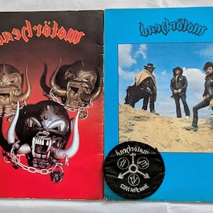 Könnte beinhalten: Zwei Albumcover und ein Patch der Band Motörhead. Ein Cover ist rot mit einem Totenkopf-Design und dem Bandnamen. Das andere ist blau mit einem Foto der Band. Der schwarze Patch zeigt den Namen und das Logo der Band.