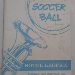 Può includere: Un opuscolo bianco con un disegno a linee blu di un pallone da calcio e uno strumento a fiato in ottone. Il testo riporta SOCCER BALL, HOTEL LEOFRIC e TUESDAY, 30th OCTOBER, 1962. Il design include una fascia orizzontale blu nella parte inferiore.